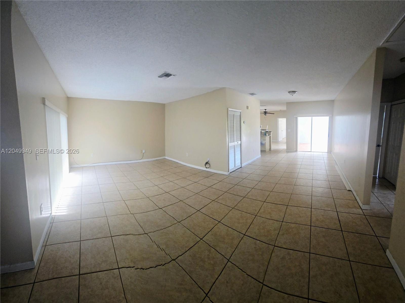 An empty living area features beige walls, tan tile flooring, and a prominent floor crack — 14236 SW 148th Ave, Miami FL 33196, MIAMI, FL