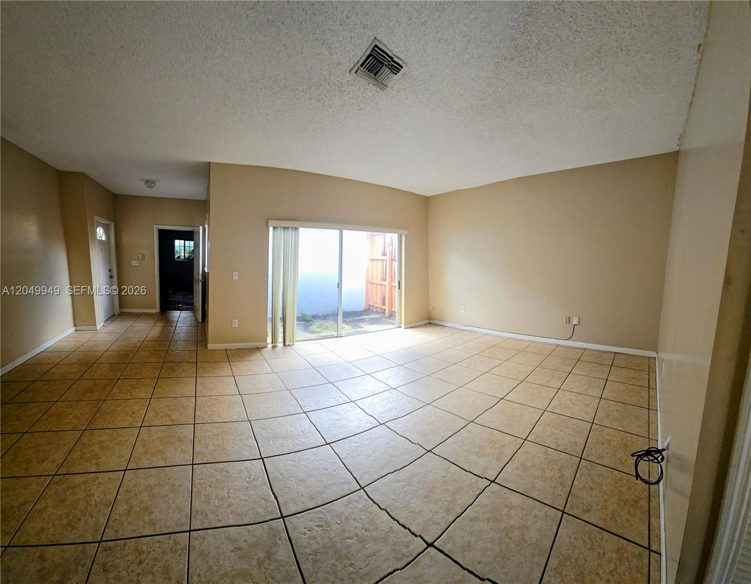 An empty living room features beige tile flooring, tan walls, and a sliding glass door — 14236 SW 148th Ave, Miami FL 33196, MIAMI, FL
