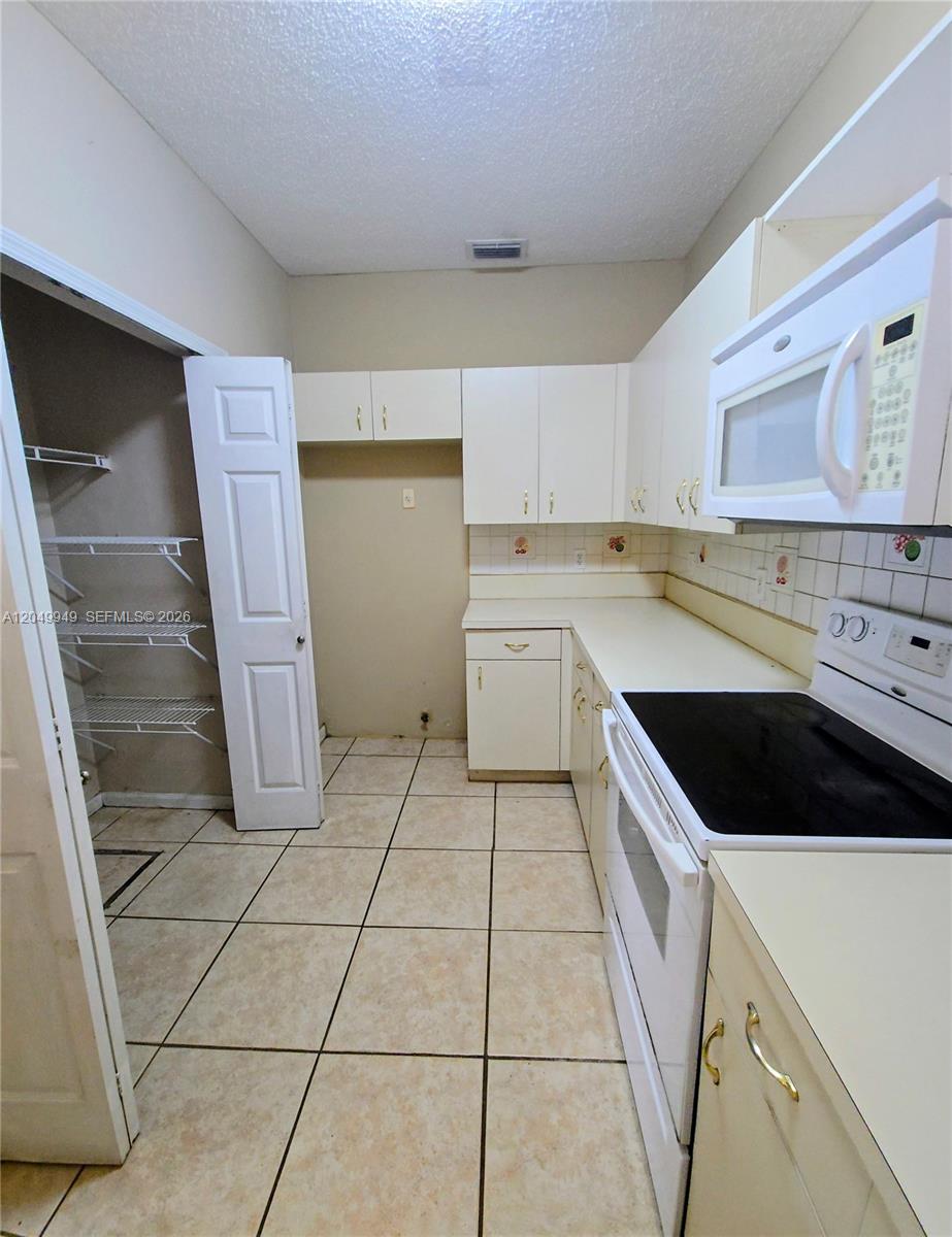 A kitchen features white cabinets, a black electric stove, a microwave, and a pantry closet — 14236 SW 148th Ave, Miami FL 33196, MIAMI, FL