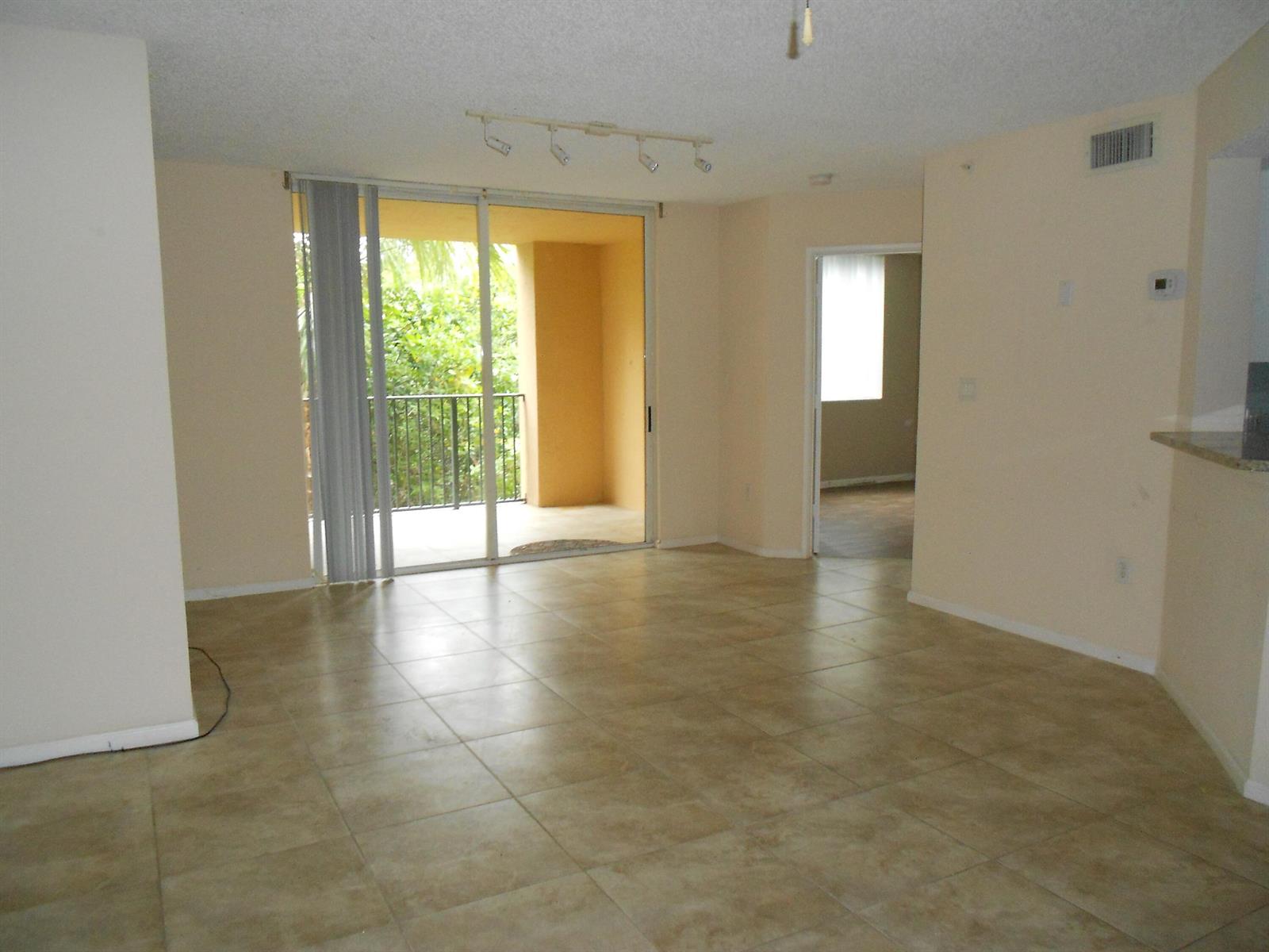 An empty living room with beige tile floors, a sliding glass door, and a balcony — 300 Scotia Drive # 203, Hypoluxo FL 33462, HYPOLUXO, FL