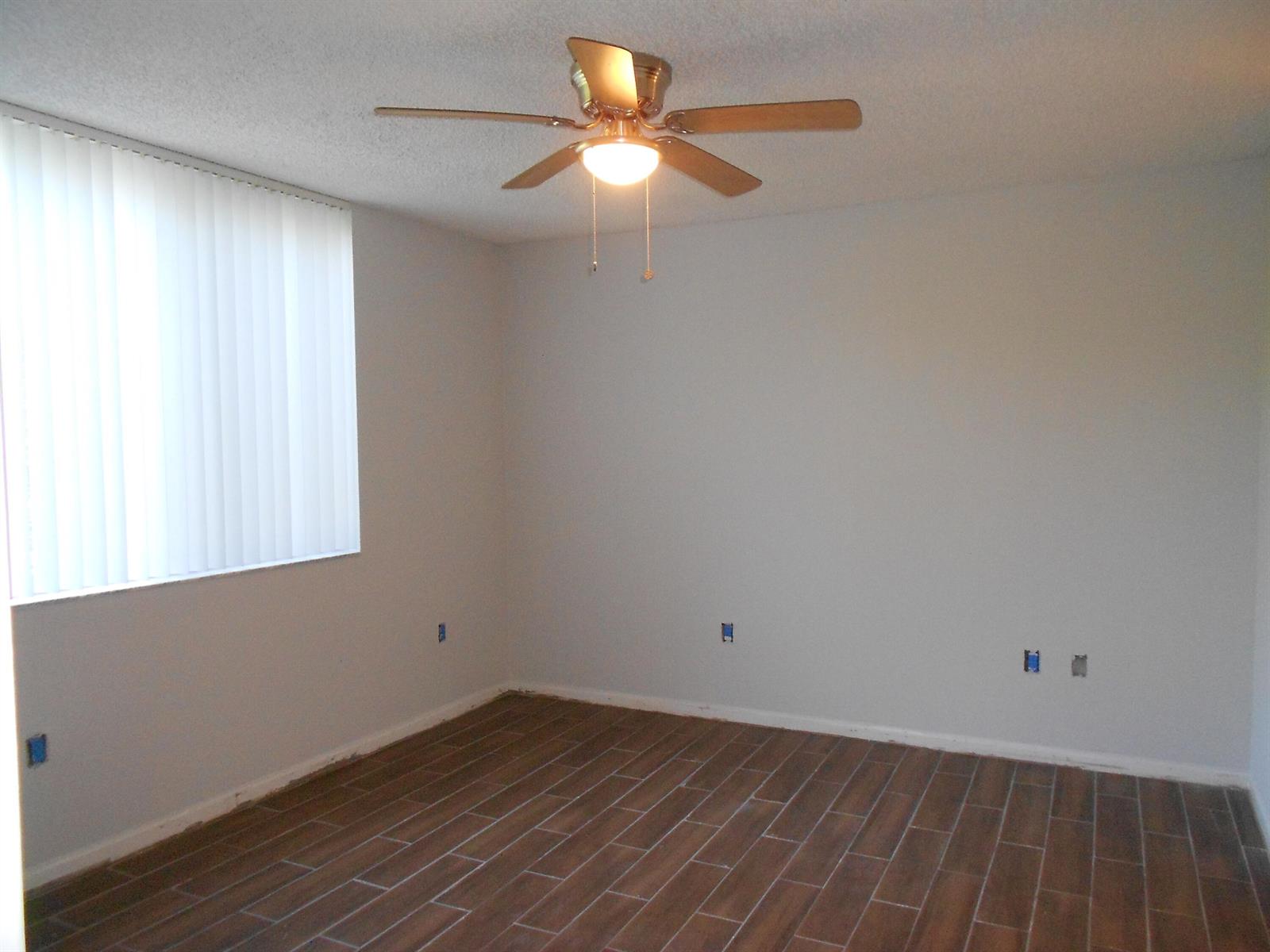 An empty room features wood-look tile flooring, white walls, a ceiling fan, and vertical blinds — 300 Scotia Drive # 203, Hypoluxo FL 33462, HYPOLUXO, FL