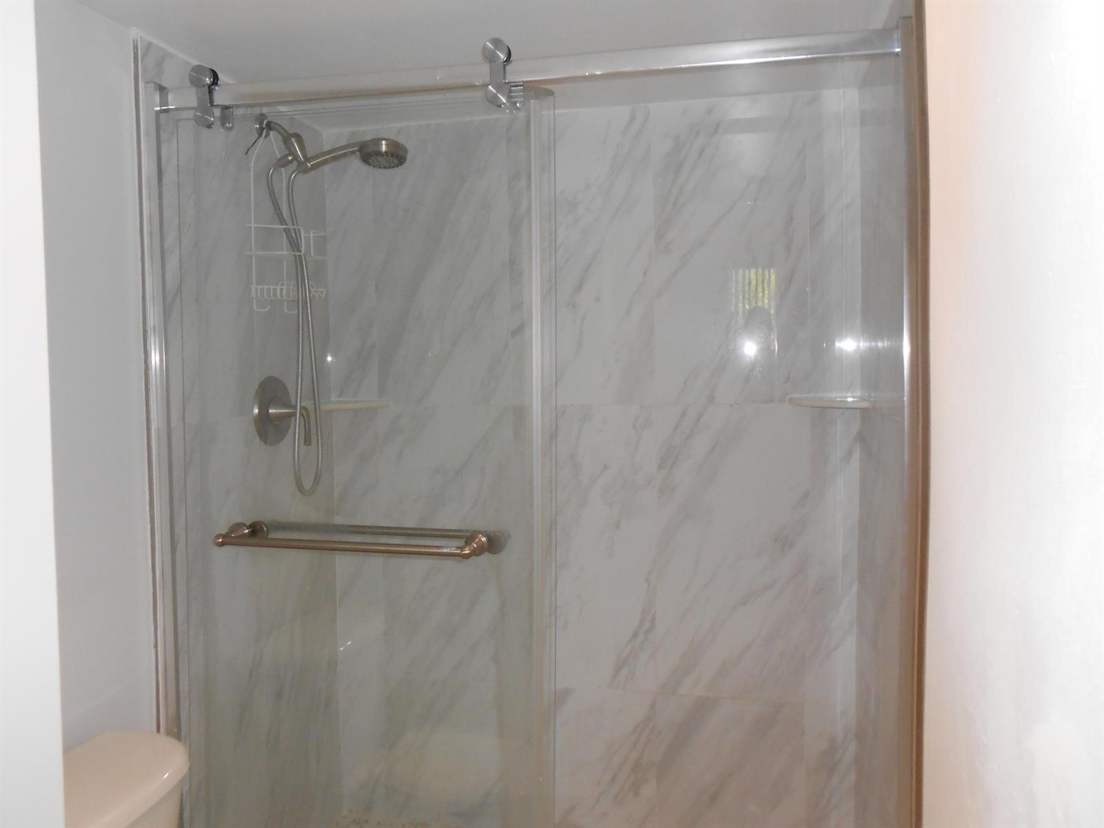 A walk-in shower features marble-look tile walls, a glass sliding door, and a handheld showerhead — 300 Scotia Drive # 203, Hypoluxo FL 33462, HYPOLUXO, FL