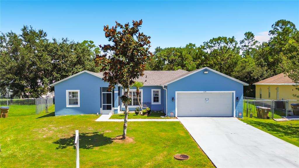 A blue single-story house with a white garage door and a front yard with trees — 1124 DARTFORD DRIVE, KISSIMMEE, FL