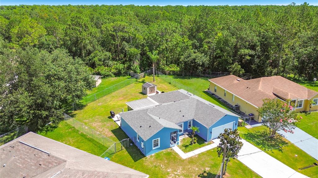 An aerial view shows a blue house with a fenced backyard bordering a wooded area — 1124 DARTFORD DRIVE, KISSIMMEE, FL