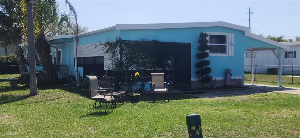 A bright blue mobile home features a side carport, a lattice privacy screen, and lawn chairs — 324 CALLE LIANA, ENGLEWOOD, FL