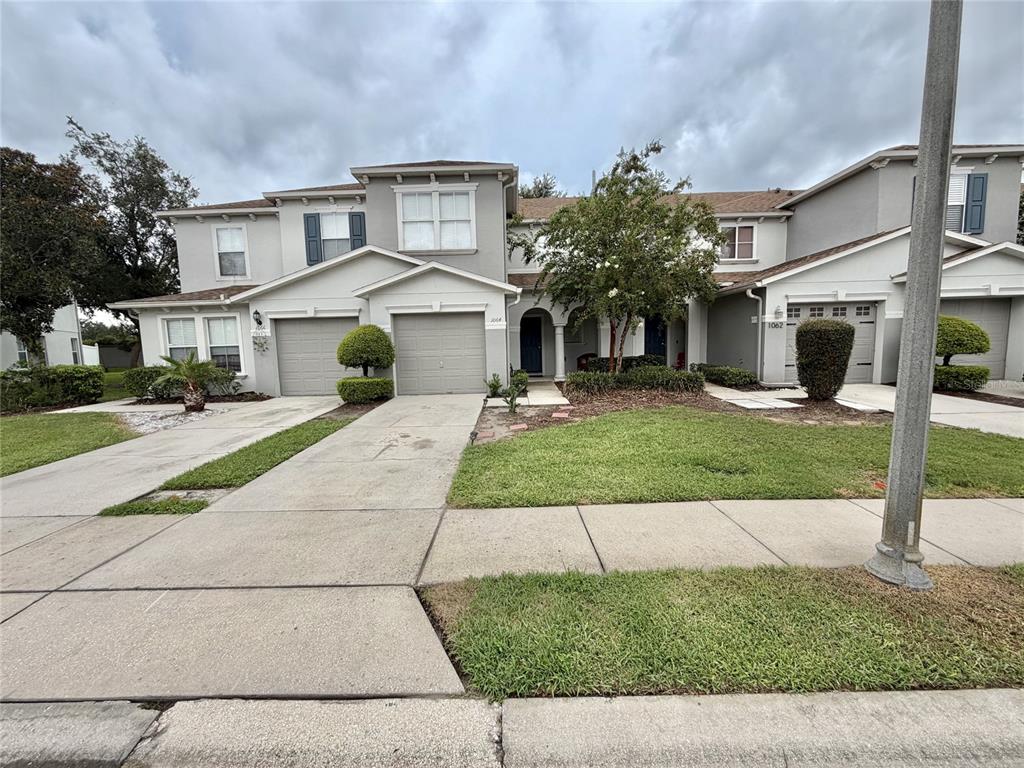 A multi-unit residential building with gray stucco siding, attached garages, and a shared front lawn — 1064 CHALCEDONY STREET, KISSIMMEE, FL