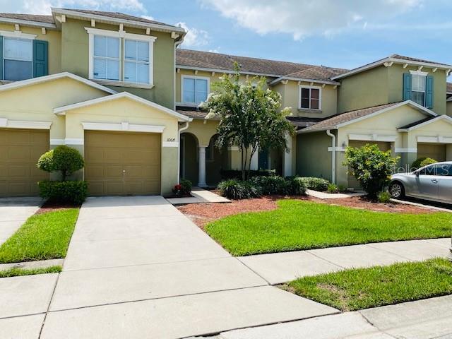 A two-story townhouse with tan siding, a two-car garage, and a small front lawn — 1064 CHALCEDONY STREET, KISSIMMEE, FL