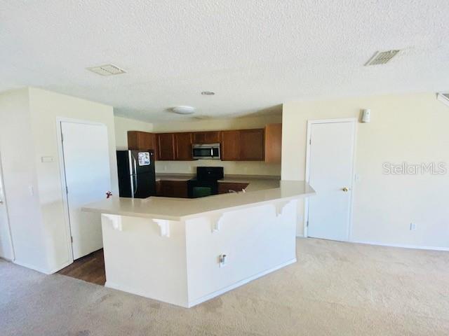 A kitchen with wood cabinets and a breakfast bar overlooks a carpeted living area — 1064 CHALCEDONY STREET, KISSIMMEE, FL