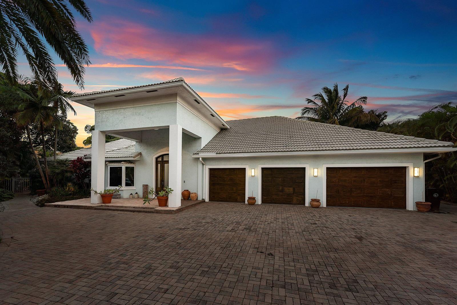 A light-colored house with a three-car garage and a paved driveway at sunset — 2311 NE 47th Street, Lighthouse Point FL 33064, LIGHTHOUSE POINT, FL