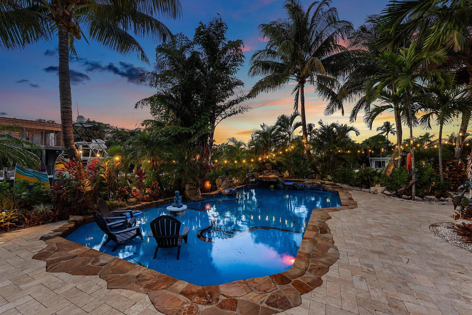A backyard swimming pool with stone coping, lounge chairs, and palm trees at sunset — 2311 NE 47th Street, Lighthouse Point FL 33064, LIGHTHOUSE POINT, FL