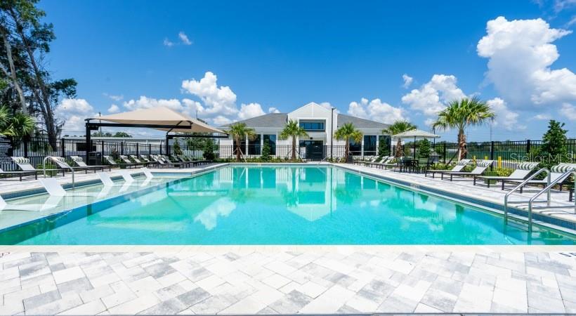 A swimming pool with lounge chairs sits in front of a community clubhouse building — 18772 GRAND LIVE OAK BOULEVARD UNIT A2.1, LAND O LAKES, FL