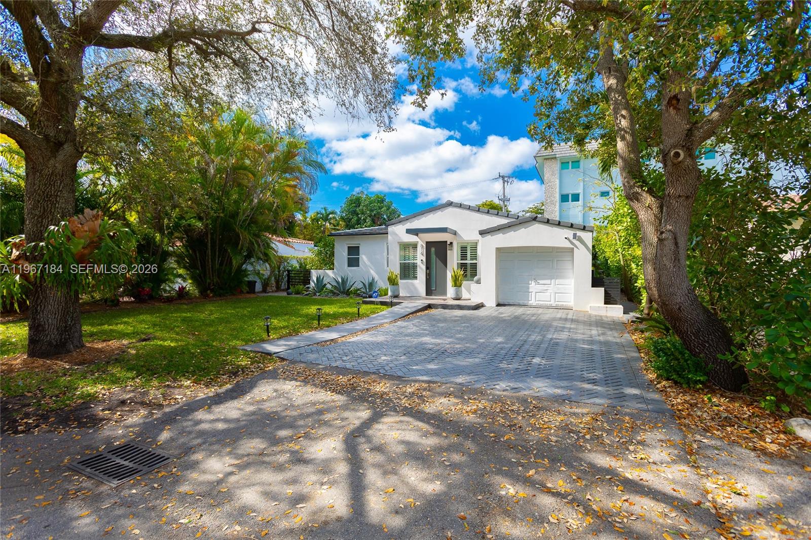 A white single-story house with a paved driveway and a garage sits among trees — 814 Monterey St, Coral Gables FL 33134, CORAL GABLES, FL