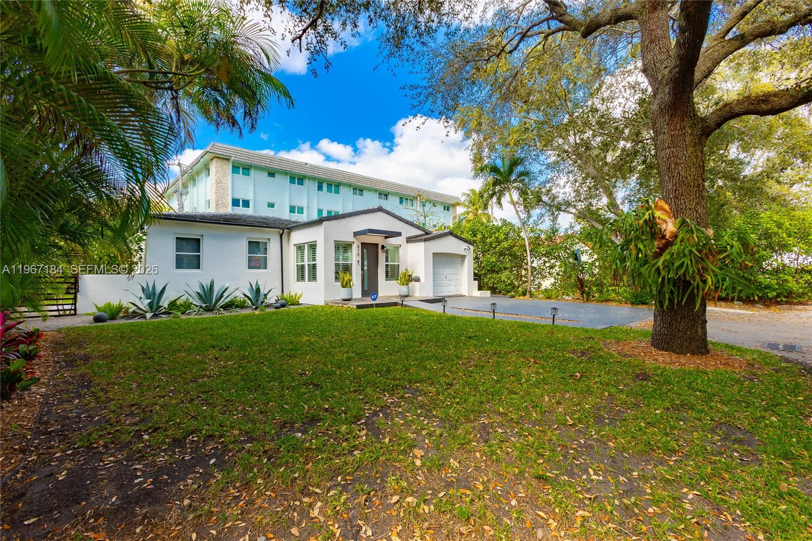 A white single-story house with a garage sits in front of a multi-story apartment building — 814 Monterey St, Coral Gables FL 33134, CORAL GABLES, FL