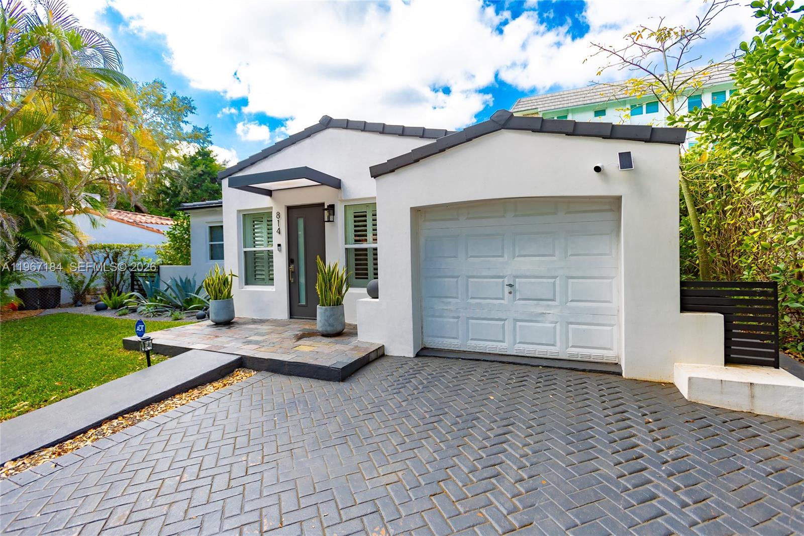 A white single-story house features a gray tiled roof, a garage, and a stone entryway — 814 Monterey St, Coral Gables FL 33134, CORAL GABLES, FL