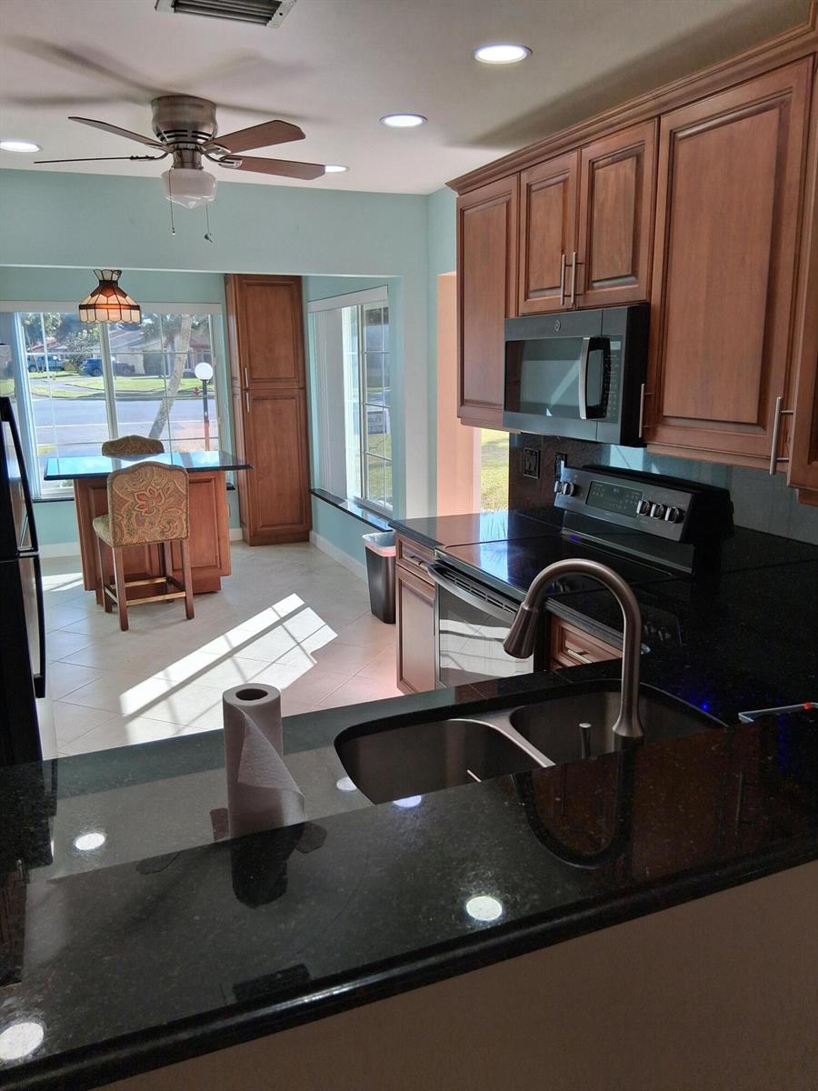 A kitchen with dark granite countertops, wood cabinets, and an adjacent dining area with windows — 4703 Rainbow Drive, FL 33463, FL