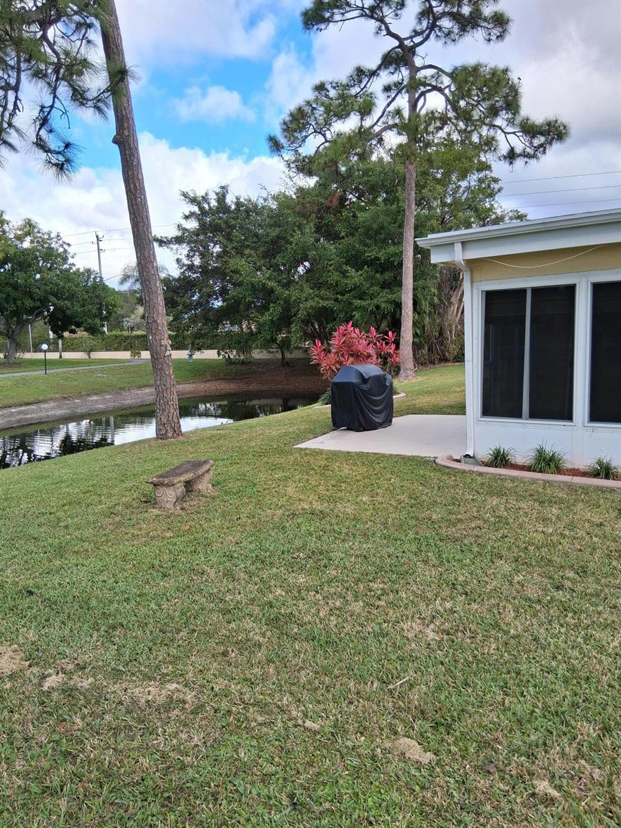 A backyard features a lawn, a small pond, a concrete patio, and a covered grill — 4703 Rainbow Drive, FL 33463, FL
