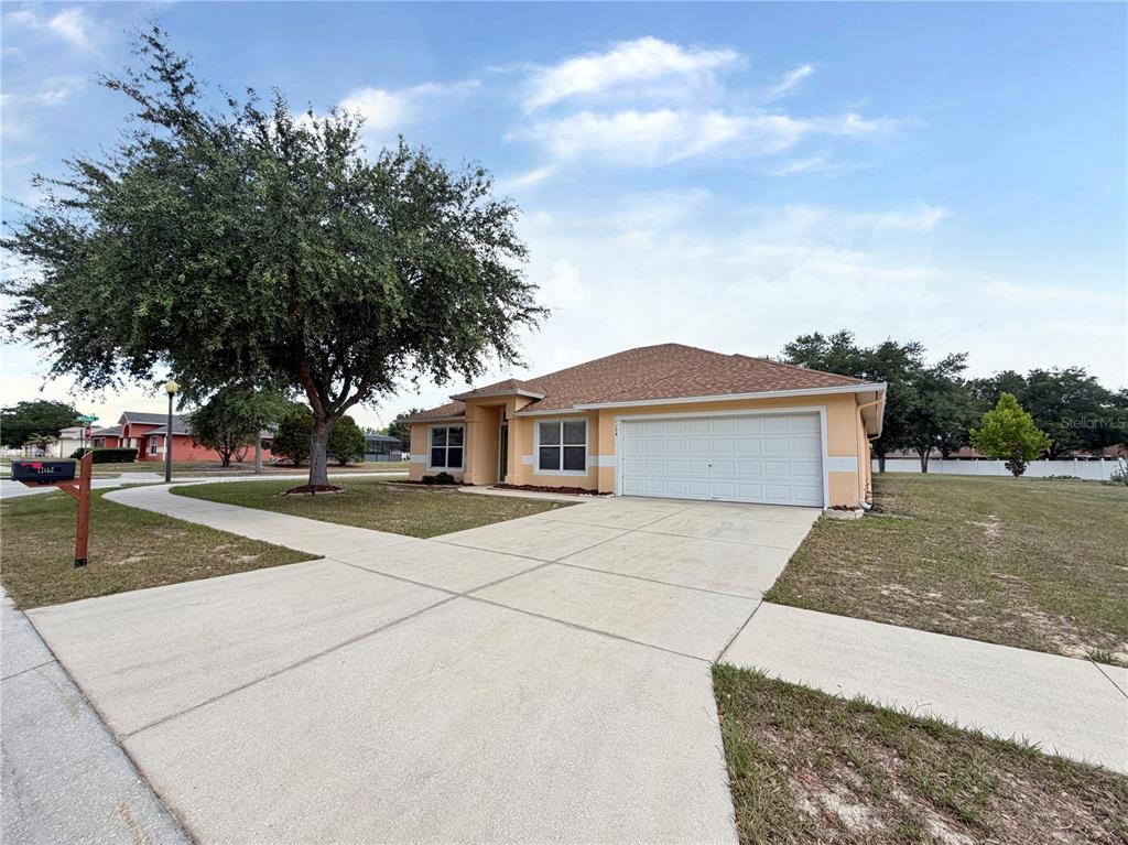 A single-story house with a beige exterior, a two-car garage, and a large front tree — 1104 STRATTON AVENUE, GROVELAND, FL