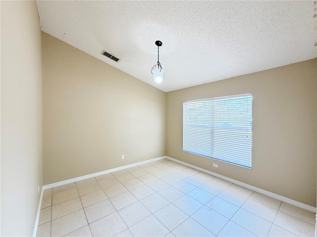 An empty room features beige walls, a vaulted ceiling, tile flooring, and a single window — 1104 STRATTON AVENUE, GROVELAND, FL