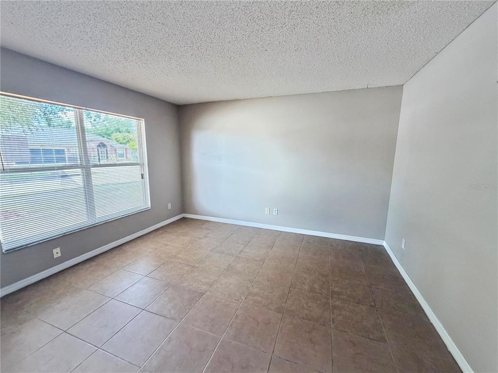 An empty room features light gray walls, brown tile flooring, and a large window — 1104 STRATTON AVENUE, GROVELAND, FL