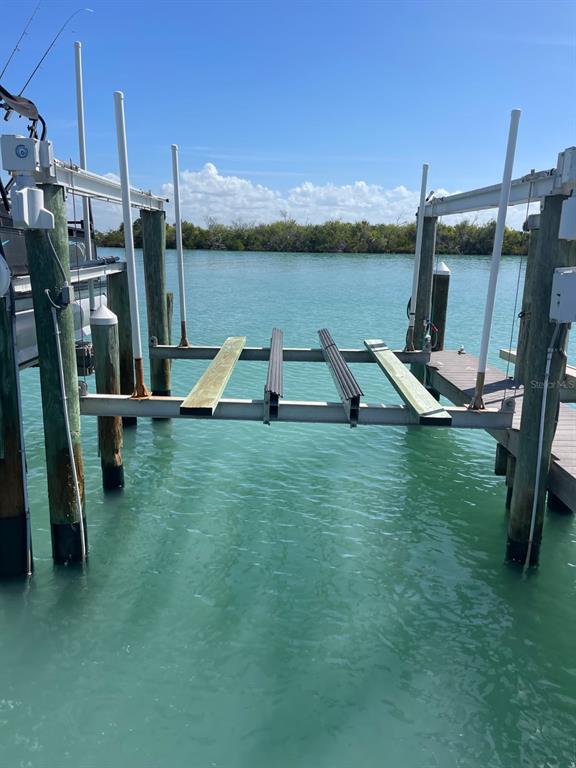 A boat lift with wooden and metal bunks sits over turquoise water between wooden pilings — 6020 BOCA GRANDE CAUSEWAY UNIT 43 Boat Slip, BOCA GRANDE, FL