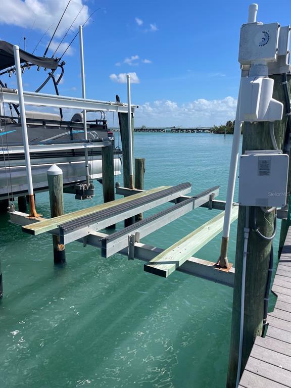 A boat lift with wooden bunks extends over turquoise water next to a docked pontoon boat — 6020 BOCA GRANDE CAUSEWAY UNIT 43 Boat Slip, BOCA GRANDE, FL