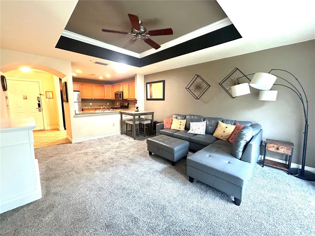 A living room with gray carpet, a sectional sofa, and an open kitchen with wood cabinets — 1310 SEVEN EAGLES COURT UNIT 201, REUNION, FL