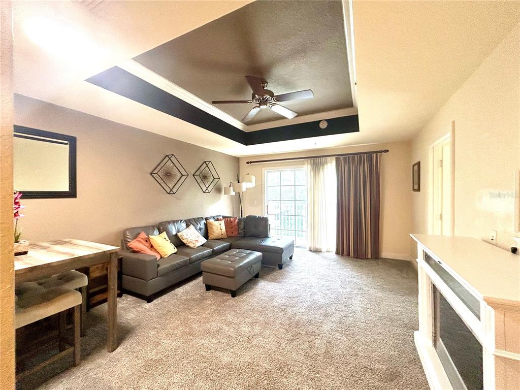 A living room features a tray ceiling, a gray sectional sofa, and a sliding glass door — 1310 SEVEN EAGLES COURT UNIT 201, REUNION, FL