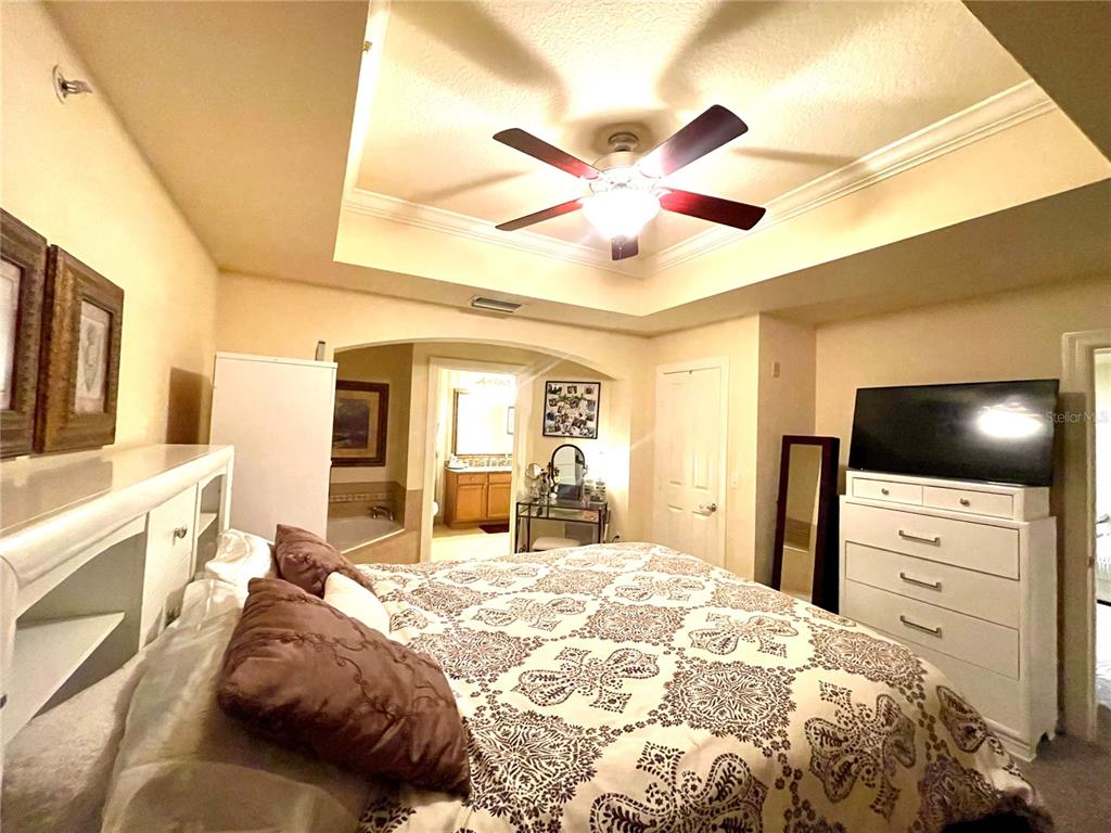 A bedroom features a tray ceiling, a ceiling fan, and a white dresser with television — 1310 SEVEN EAGLES COURT UNIT 201, REUNION, FL