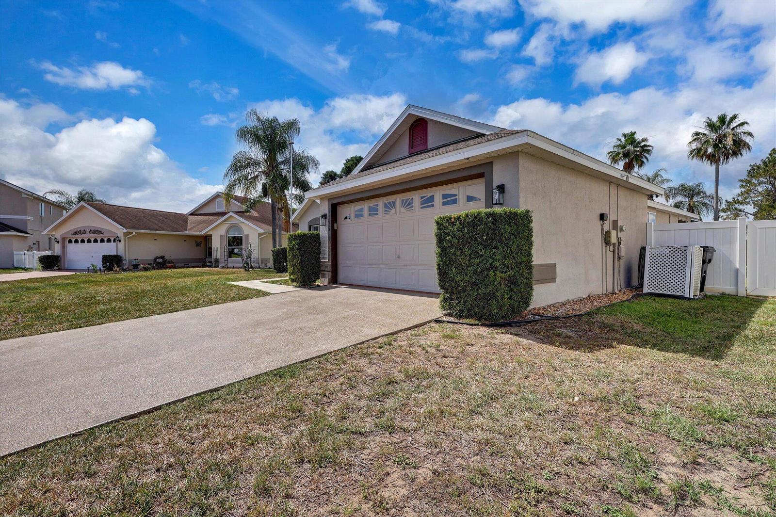 A tan house with a two-car garage and a concrete driveway under a blue sky — 1175 Jaybee Avenue, Davenport FL 33897, DAVENPORT, FL
