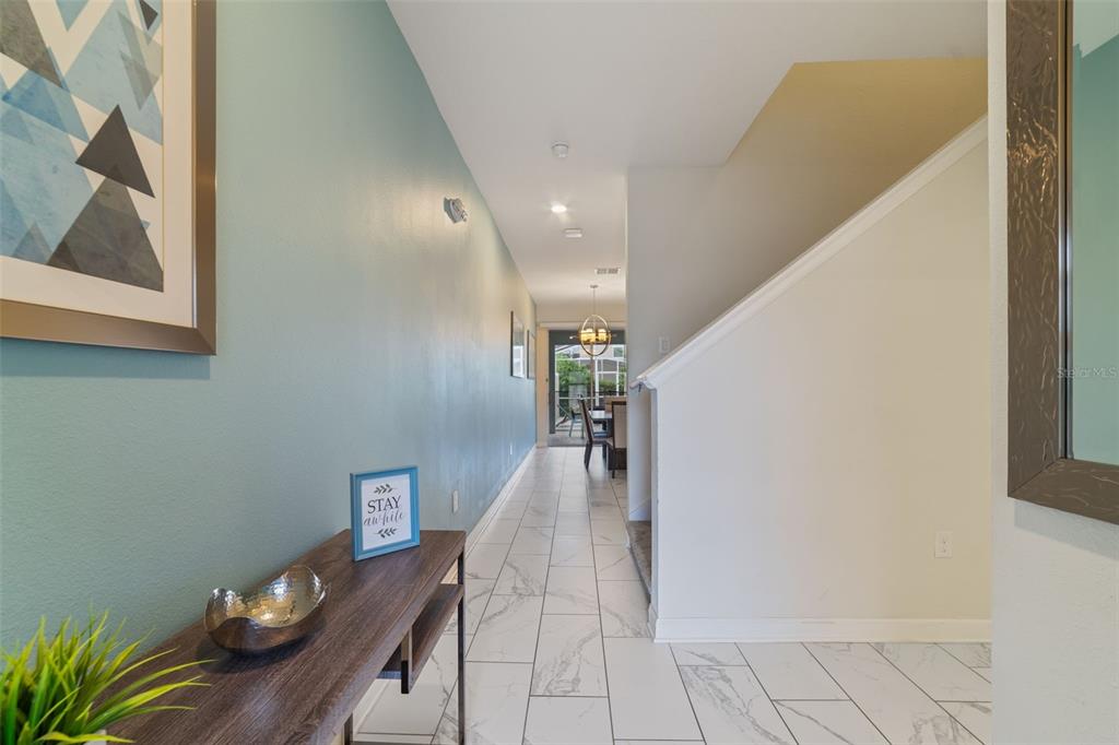 A hallway with light blue walls, white tile flooring, and a staircase leads toward a dining area — 388 OCEAN COURSE AVENUE, DAVENPORT, FL