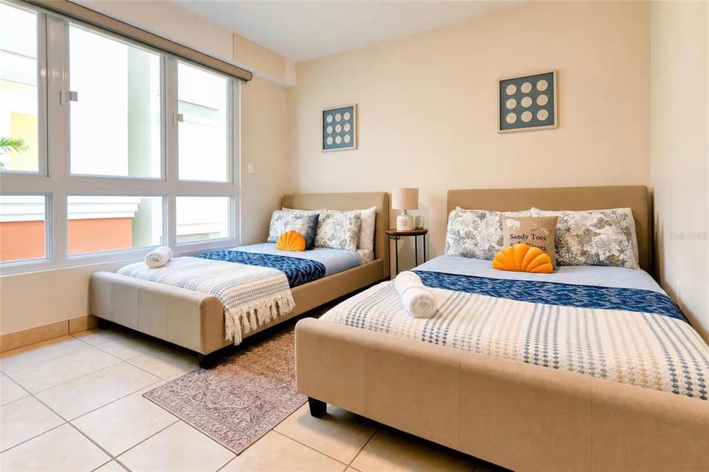 A bedroom features two beds with tan upholstered frames, patterned bedding, and large windows — 100 OCEAN DRIVE UNIT 131, HUMACAO, PR