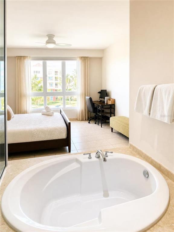 A bedroom features a large soaking tub in the foreground and a bed near windows — 100 OCEAN DRIVE UNIT 131, HUMACAO, PR