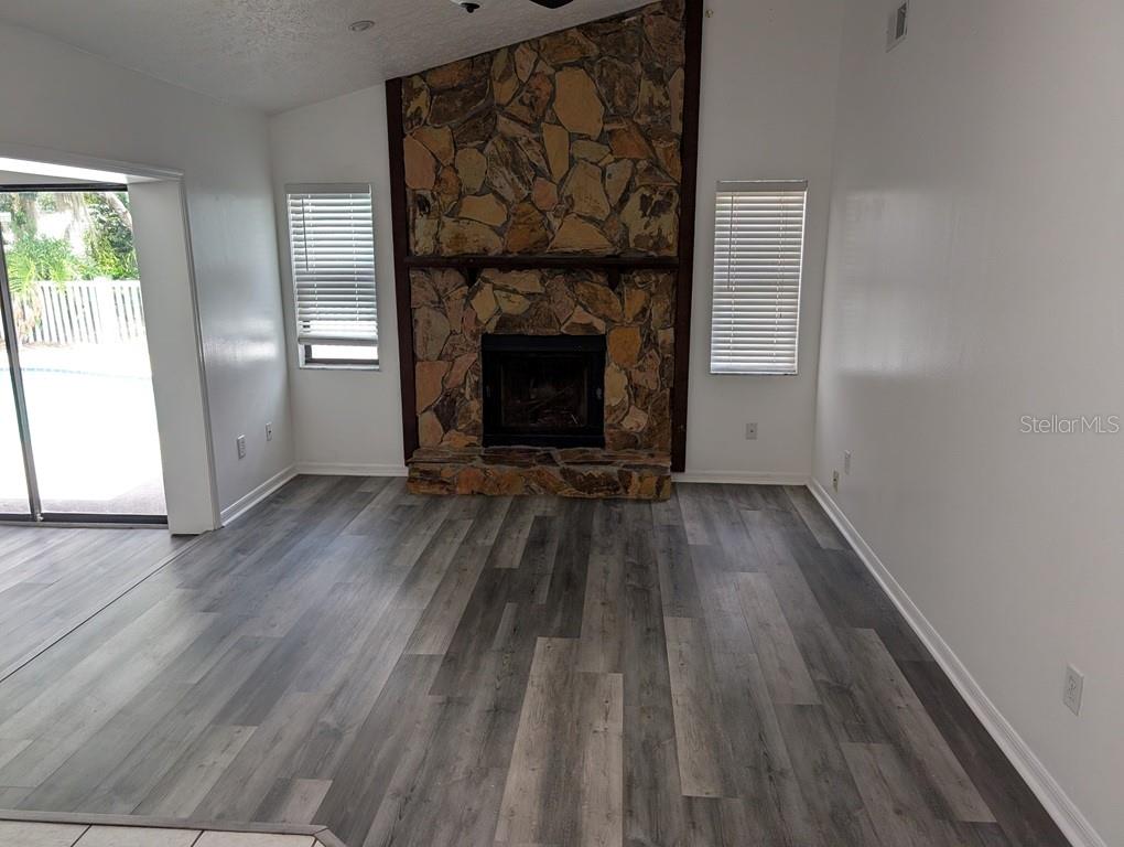A living room features a stone fireplace, wood-look flooring, and a sliding glass door — 11122 HANNAWAY DRIVE, RIVERVIEW, FL