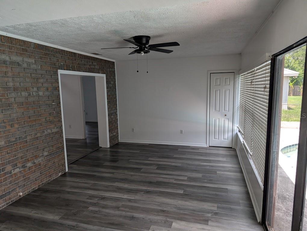 A room with gray wood-look flooring, a brick wall, a ceiling fan, and sliding glass doors — 11122 HANNAWAY DRIVE, RIVERVIEW, FL