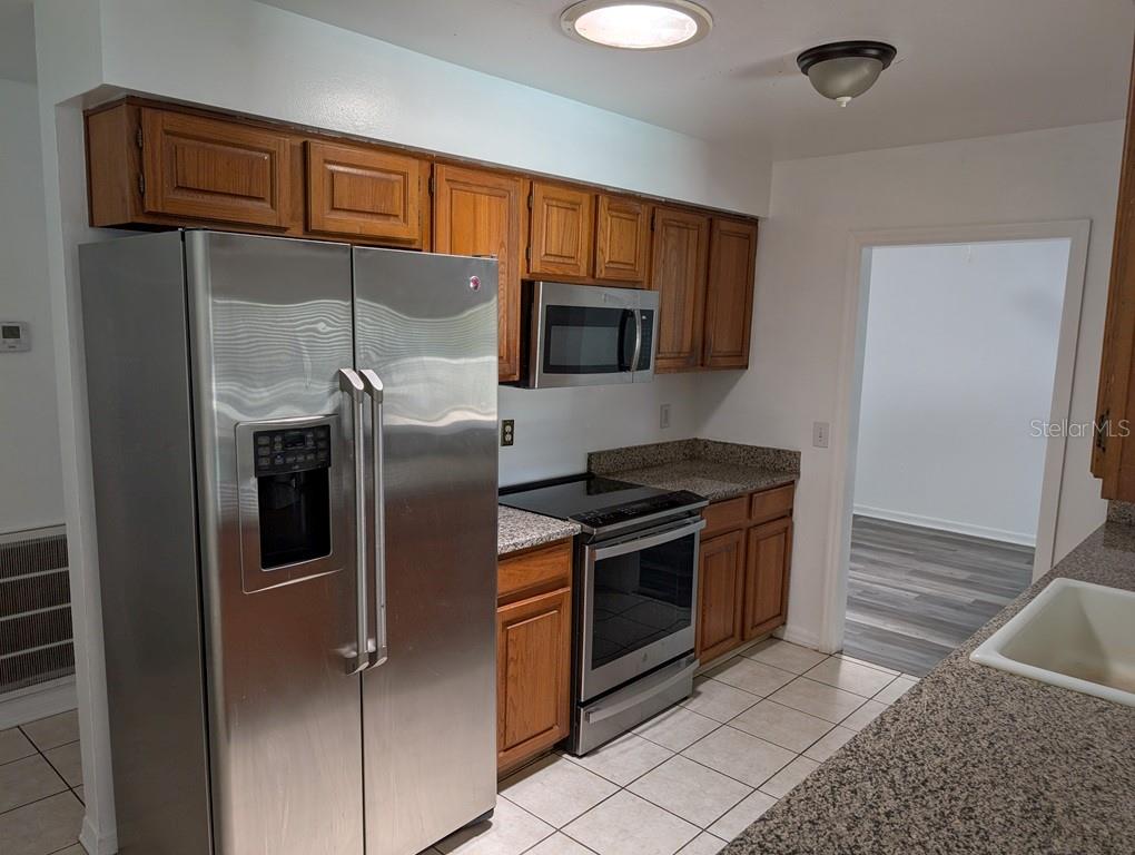 A kitchen features wood cabinets, stainless steel appliances, granite countertops, and light-colored tile flooring — 11122 HANNAWAY DRIVE, RIVERVIEW, FL