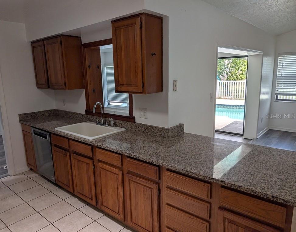 A kitchen with wood cabinets, granite countertops, a white sink, and a view of a pool — 11122 HANNAWAY DRIVE, RIVERVIEW, FL