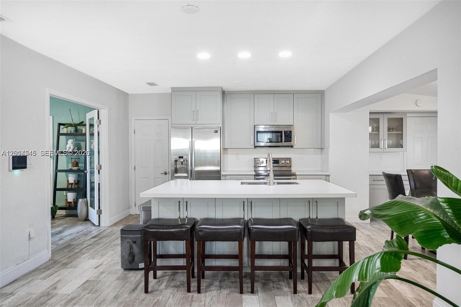 A modern kitchen features light gray cabinets, stainless steel appliances, and a central island with seating — 1946 SW 20th St # 1946, Miami FL 33145, MIAMI, FL