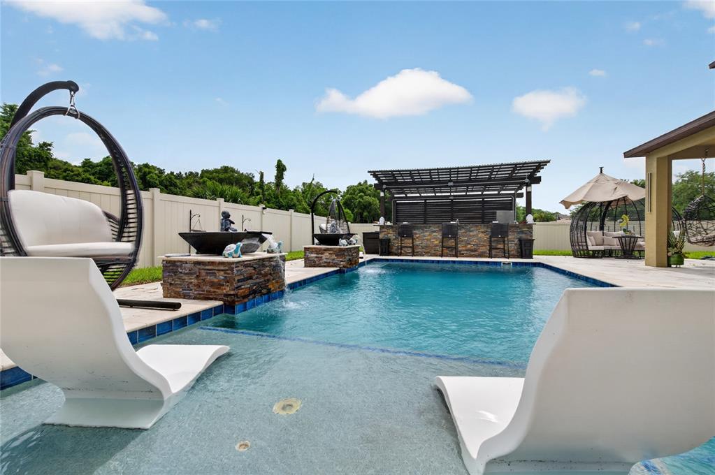 A backyard swimming pool features a tanning ledge, stone water features, and a covered bar — 1801 WATERSIDE OAKS DRIVE, ORANGE CITY, FL