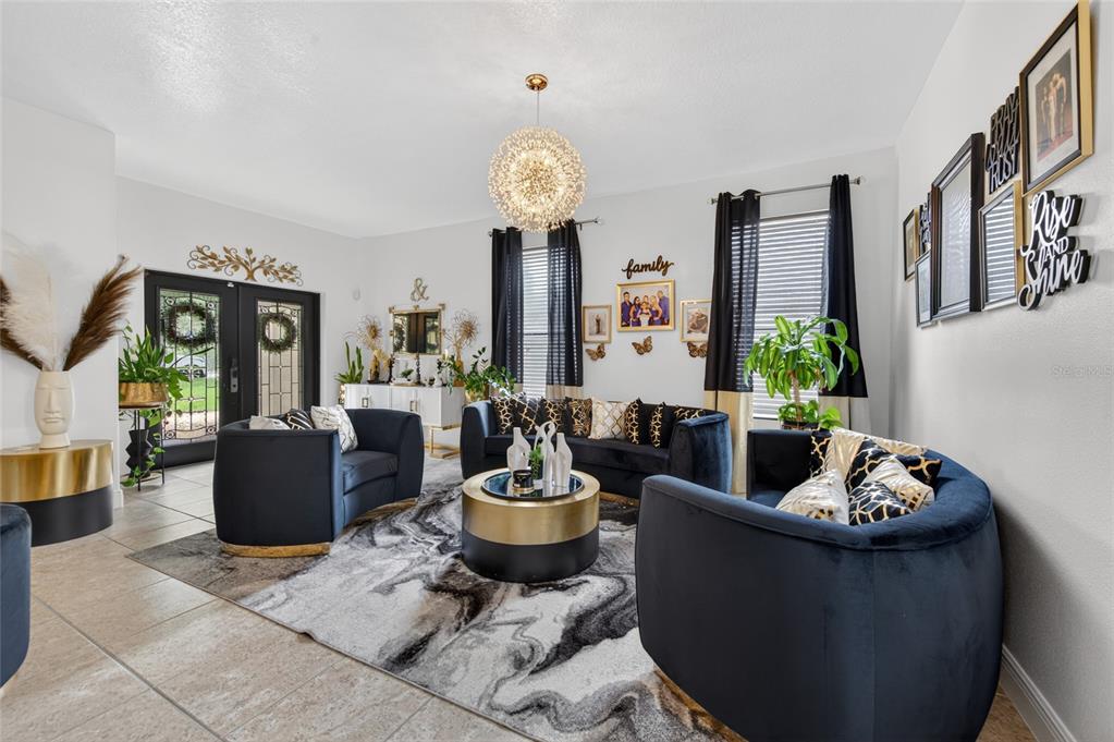 A living room features navy velvet furniture, a gold-accented coffee table, and a modern chandelier — 1801 WATERSIDE OAKS DRIVE, ORANGE CITY, FL