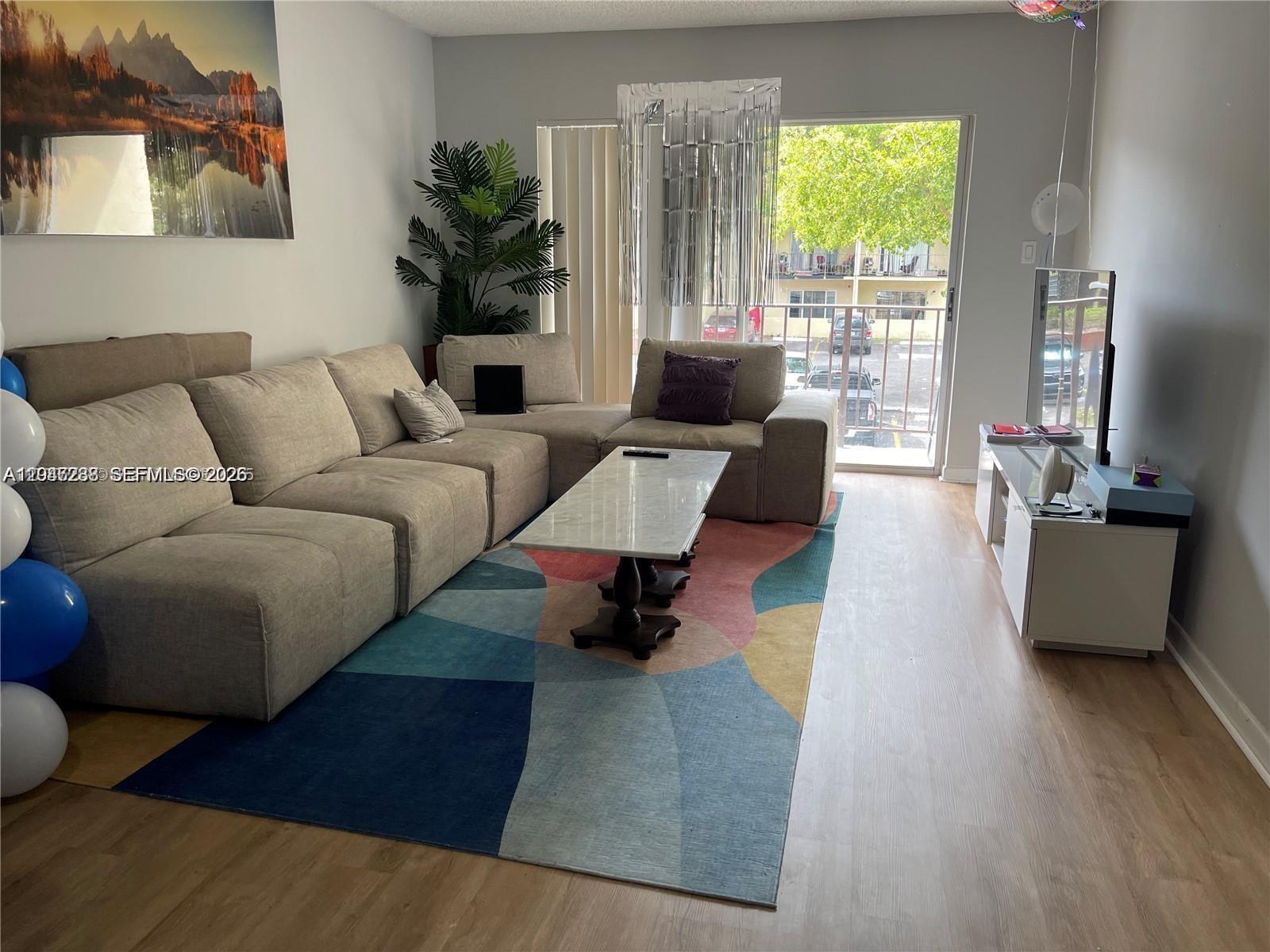 A living room features a beige sectional sofa, a colorful area rug, and a balcony — 12035 NE 2nd Ave # A209, North Miami FL 33161, NORTH MIAMI, FL
