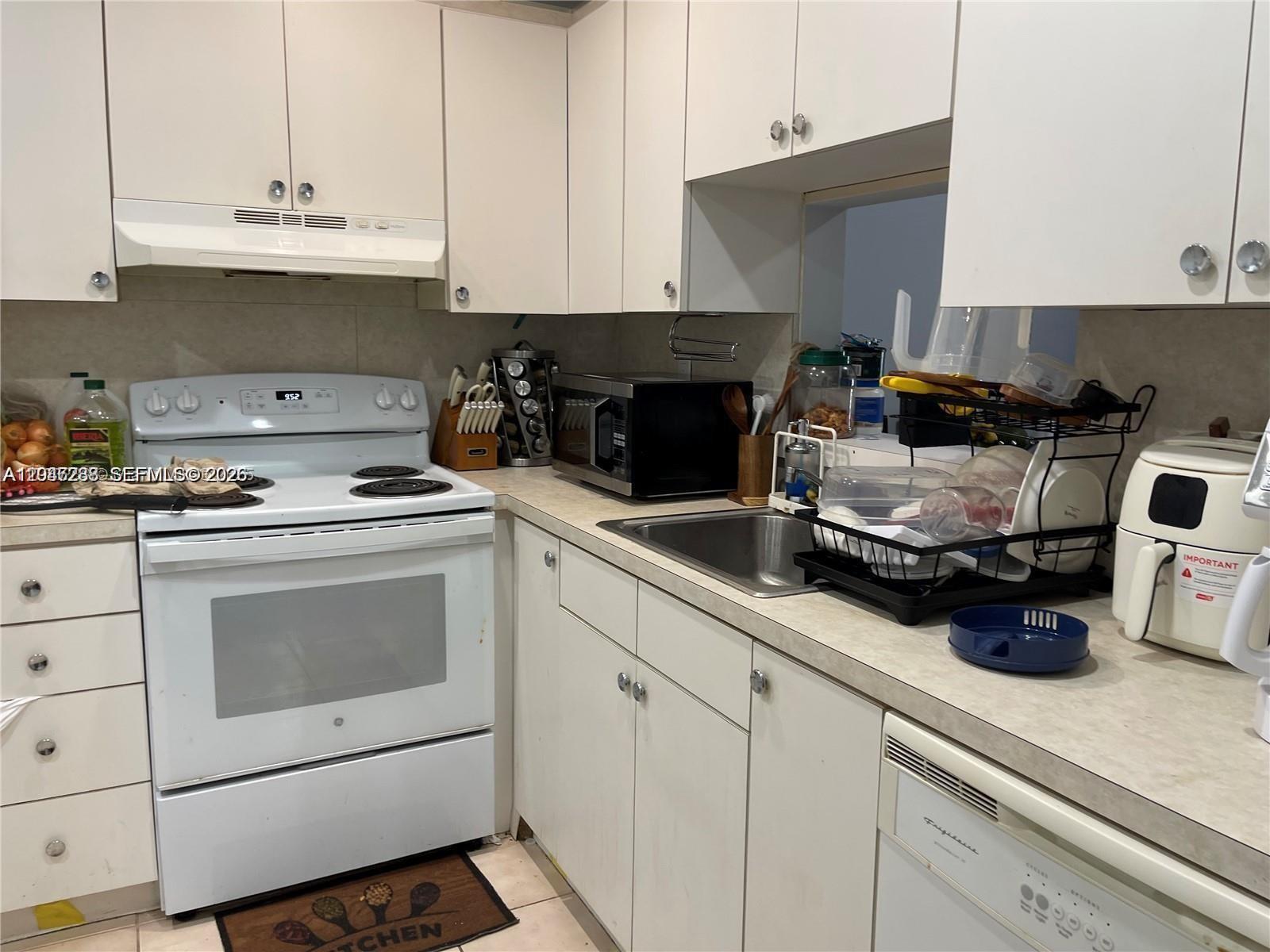 A kitchen features white cabinets, a white stove, a stainless steel sink, and a dishwasher — 12035 NE 2nd Ave # A209, North Miami FL 33161, NORTH MIAMI, FL