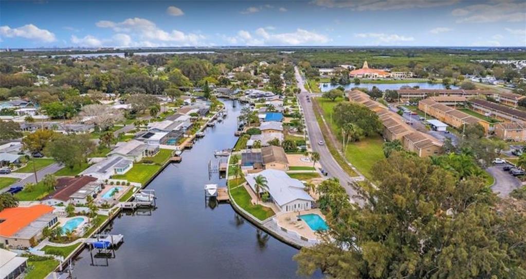 An aerial view shows a canal-front residential neighborhood with houses, swimming pools, and a road — 245 78 TH AVENUE N, ST PETERSBURG, FL