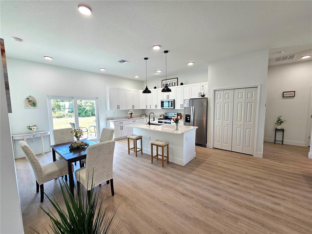 An open-concept kitchen and dining area features white cabinetry, a central island, and wood-look flooring — 2523 SW 153RD PLACE ROAD, OCALA, FL