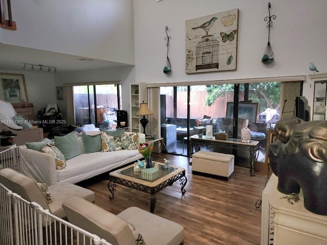 A living room features high ceilings, wood-look flooring, a white sofa, and large sliding glass doors — 11060 SW 143rd Pl, Miami FL 33186, MIAMI, FL
