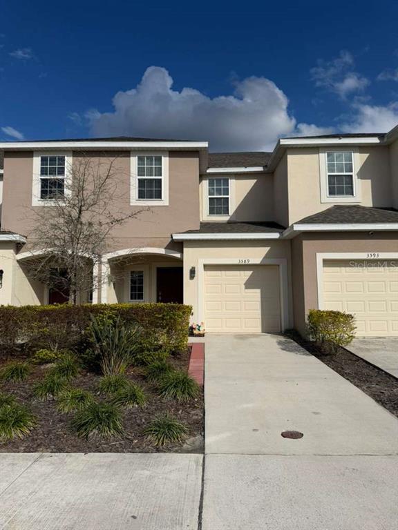 A two-story townhouse exterior with a tan facade, a single-car garage, and a small front yard — 3589 ANIBAL STREET, KISSIMMEE, FL
