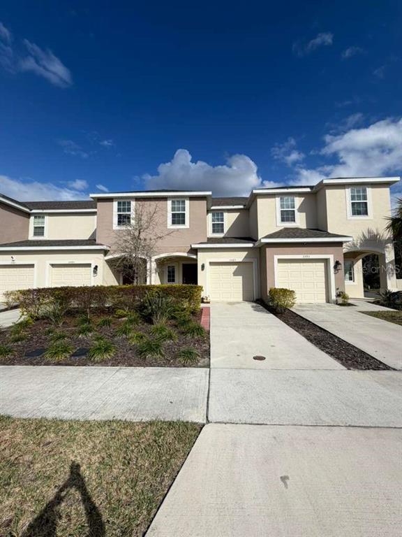 A row of two-story townhouses with beige stucco exteriors, attached garages, and concrete driveways — 3589 ANIBAL STREET, KISSIMMEE, FL