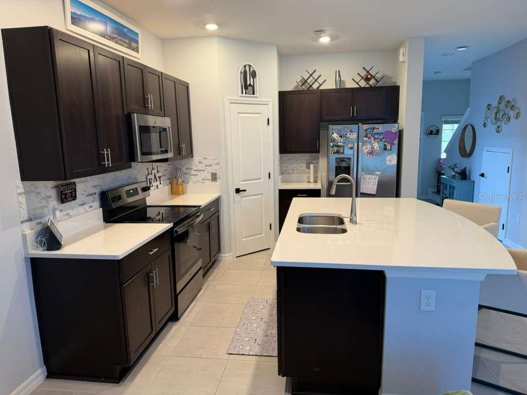 A kitchen features dark wood cabinets, white countertops, a central island, and stainless steel appliances — 3589 ANIBAL STREET, KISSIMMEE, FL