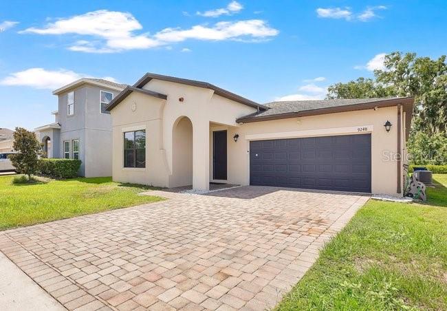 A single-story house with a beige stucco exterior, a dark garage door, and a paver driveway — 9248 CHANDLER DRIVE, GROVELAND, FL