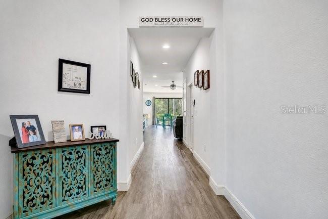 A hallway with light wood flooring leads toward a bright room with a glass door — 9248 CHANDLER DRIVE, GROVELAND, FL
