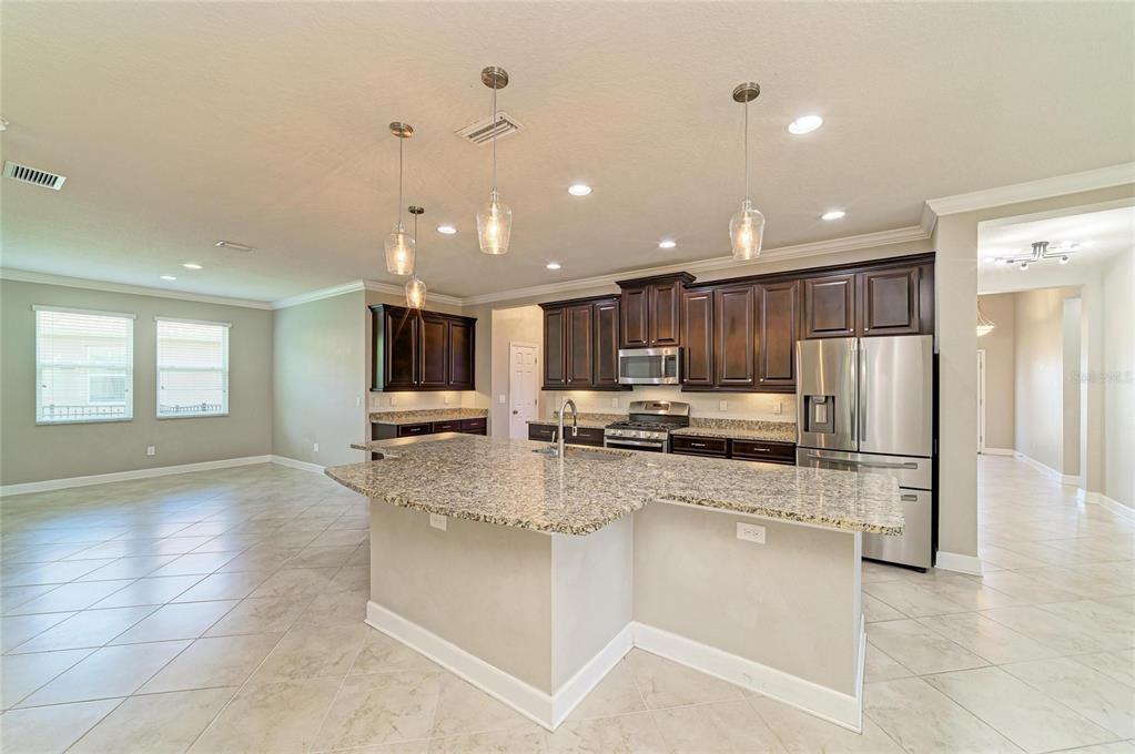 A kitchen with dark wood cabinets, granite countertops, a large island, and tile flooring — 12821 BALSAM TERRACE, BRADENTON, FL